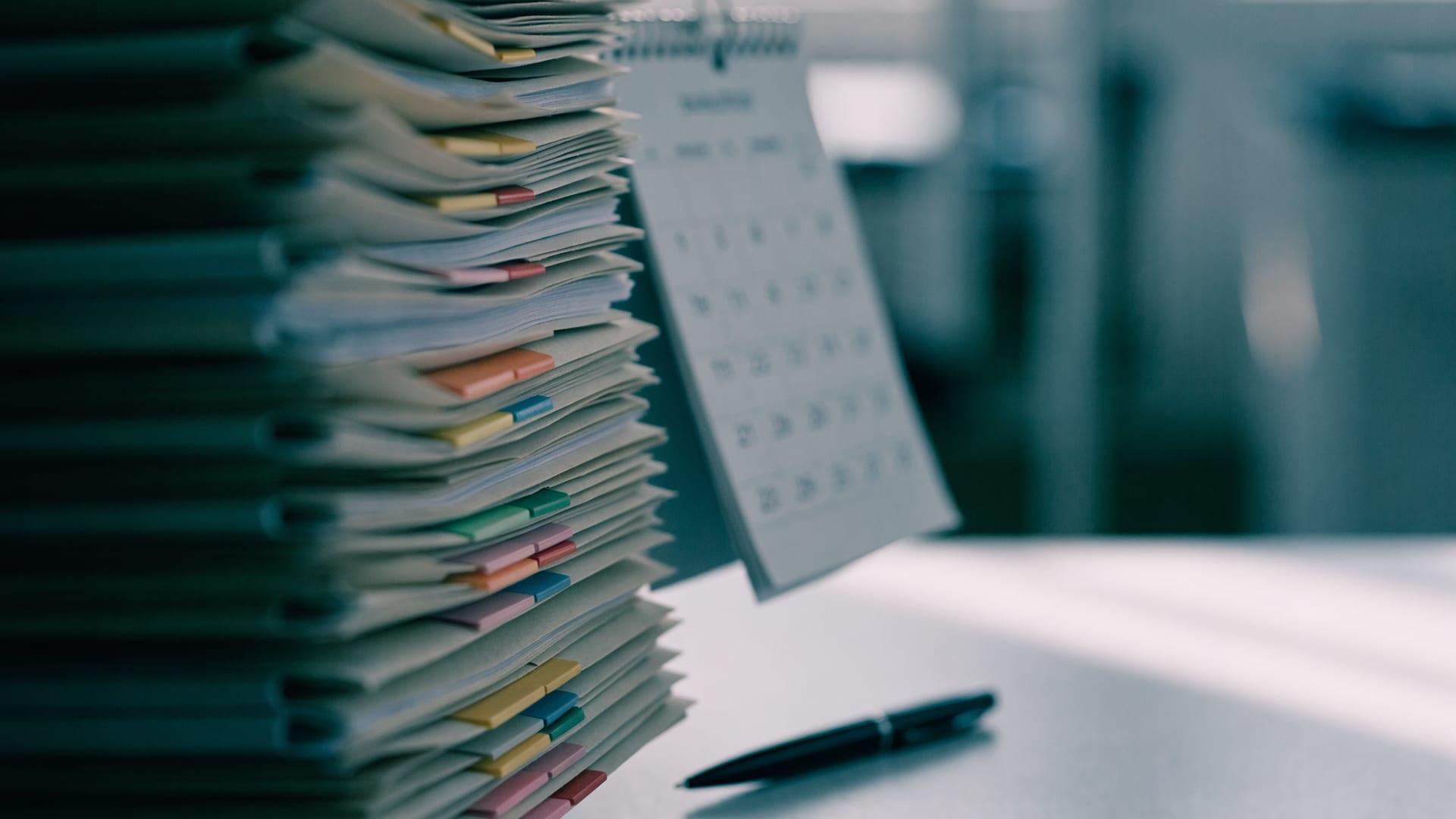 A stack of tabbed document folders beside a wall calendar